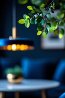 Fresh green leaves frame modern restaurant interior with blue velvet seating and soft pendant lighting, creating atmospheric dining ambiance.