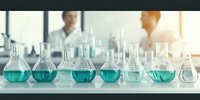 Laboratory glassware with turquoise chemical solutions on white table. Scientists working in blurred background. Research and development concept.