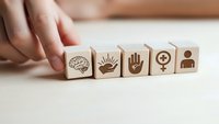 Hand arranging wooden blocks with human resource icons including brain, eye, hand, gender symbol and person on white surface for business concepts.