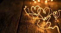 Warm golden heart-shaped fairy lights glowing on rustic wooden surface creating romantic atmosphere for Valentine's Day celebrations and love themes.