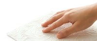 Hand touching embossed white paper with floral pattern texture for tactile sensory experience and braille reading concept.