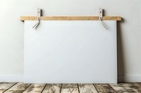 Blank white canvas mockup hanging on wooden clips against light wall, rustic wooden floor beneath. Ready for art and design presentation display.