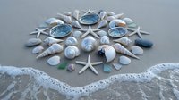 Seashells, starfish and sea glass arranged in mandala pattern on sandy beach with ocean waves. Coastal meditation and mindfulness concept for relaxation.