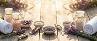 Dried lavender buds in bowls and glass jars with rolled towels on wooden surface for spa, wellness, aromatherapy and natural beauty product applications.