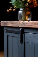 Modern farmhouse cabinet with sliding barn door hardware and rustic wood countertop, decorated with glass vase holding autumn berries against dark background.