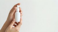 Close-up of female hand holding white spray bottle against neutral background, suitable for skincare, cosmetics, cleaning products, and beauty packaging mockups.