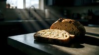 Freshly baked artisan bread loaf with seeds sliced on dark surface in natural sunlight, suitable for bakery, food, and culinary design projects.
