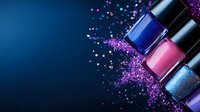 Colorful nail polish bottles with scattered glitter on dark blue background. Luxury cosmetics and beauty products arrangement with sparkles and shimmer effects.