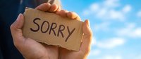 Hands holding cardboard sign with sorry message against blue sky background. Apology concept for forgiveness, reconciliation and emotional healing.