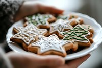 Freshly baked gingerbread cookies with white icing decoration in star and Christmas tree shapes served on white plate, selective focus on holiday treats.