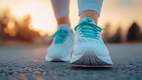 Running shoes on asphalt road during golden sunset, close-up view of turquoise athletic footwear with mesh texture and laces against blurred background.