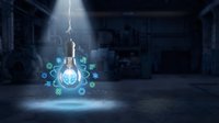 Glowing light bulb with digital technology icons floating in dark industrial warehouse with dramatic lighting beam from above.