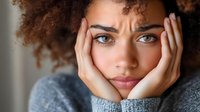 Young mixed-race woman with curly hair resting chin on hands looking thoughtful and contemplative with natural lighting for lifestyle content.
