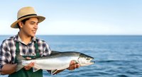 Man in straw hat holding fresh caught fish at sea. Fisherman displaying salmon for commercial fishing, seafood industry, or recreational angling content.