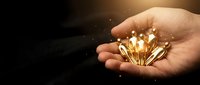 Hand holding glowing golden light bulbs with sparkling effects against dark background symbolizing innovation creativity and bright ideas for business.