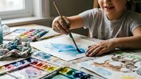 Young Asian girl painting watercolor artwork at home table with brushes and art supplies for creative education and artistic development.