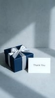 Navy blue gift box with white satin ribbon bow and thank you card on gray concrete surface with soft natural light and shadows.