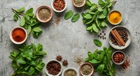 Fresh herbs and aromatic spices arranged in wooden bowls on rustic concrete surface for culinary cooking and seasoning recipes.