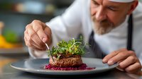 Professional chef garnishing gourmet meat dish with fresh microgreens in commercial kitchen. Culinary artistry and fine dining presentation for restaurants.