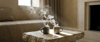 Cozy living room interior with steaming coffee mugs on rustic wooden table near fireplace creating warm atmosphere for relaxation and comfort at home.
