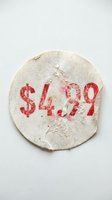 Worn round price sticker with red dollar amount on textured paper surface, peeling and aged, isolated on white background.