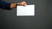Male hand holding blank white card or paper against gray background for mockup and branding purposes.