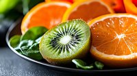 Sliced kiwi and orange fruits arranged on a black plate with fresh green leaves, showcasing vibrant tropical produce for food and nutrition content.