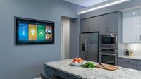 Modern smart kitchen with interactive touchscreen display mounted on wall showing colorful app interface tiles for home automation and cooking.