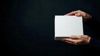 Person with medium skin tone holding blank white card or paper against dark background, suitable for mockups, advertising, and promotional materials.