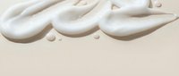 Creamy white cosmetic texture with smooth flowing waves and droplets on neutral beige background for skincare and beauty product applications.