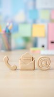 Wooden contact icons phone envelope email symbol on desk with blurred office background representing customer service and business communication.