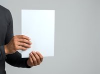 Man in dark shirt holding blank white paper sheet for mockup or presentation purposes against neutral gray background.