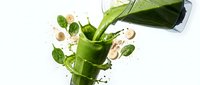 Green smoothie splash with spinach leaves and nuts flying from blender jar on white background for healthy nutrition and diet concepts.