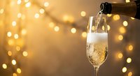Champagne pouring into elegant flute glass with golden bokeh lights background for celebration and festive occasions.