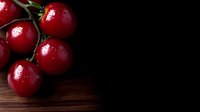 Fresh ripe red cherry tomatoes with water drops on dark wooden background, dramatic lighting creates moody food composition for restaurant menu design.
