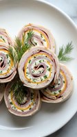 Ham and cheese pinwheel sandwiches with fresh dill garnish served on white plate for lunch, appetizers, catering, food photography, and culinary content.