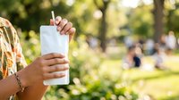 Woman holding blank white tumbler with straw outdoors in park, mockup for beverage branding, summer refreshment marketing.