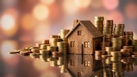 Wooden house model surrounded by golden coins with warm bokeh lights background representing real estate investment and property savings concept.