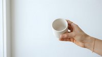 Male hand holding empty white ceramic mug against neutral background, suitable for beverage branding, mockup designs, and product marketing campaigns.