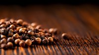 Fresh allspice peppercorns scattered on dark rustic wooden surface with selective focus and warm lighting, creating aromatic culinary atmosphere.