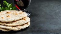 Fresh homemade flatbread stack with red wine glass on dark background. Traditional naan or pita bread for Mediterranean and Indian cuisine.