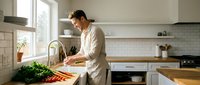 Man in casual beige shirt preparing fresh vegetables at kitchen sink with white subway tile backsplash and wooden countertops, ideal for cooking and lifestyle content.