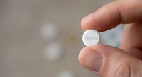 Hand holding white placebo pill between fingers against blurred medical background for pharmaceutical research and clinical trial concepts.