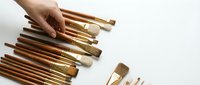 Artist hand arranging professional paint brushes with wooden handles on white background, top view of art supplies collection for painting.
