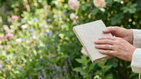 Woman holding open blank notebook outdoors in spring garden with blooming flowers, suitable for education, journaling, writing, and lifestyle content.