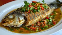 Grilled whole fish with colorful bell peppers, herbs and savory sauce on white plate. Fresh seafood dish with vibrant vegetables for restaurant menu.