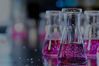 Laboratory glassware with bright pink liquid and bubbles against dark background shows scientific research and chemical experimentation in modern lab setting.