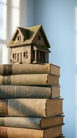 Miniature wooden house model sitting on stack of vintage books symbolizing knowledge, education, real estate investment and home ownership dreams.