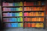 Colorful bookshelf with books arranged in rainbow spectrum order from pink to orange, creating vibrant gradient display in wooden bookcase.