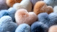 Soft fluffy fur pom poms in pastel pink, peach and blue colors arranged in rows creating gentle textural background pattern for fashion and design projects.